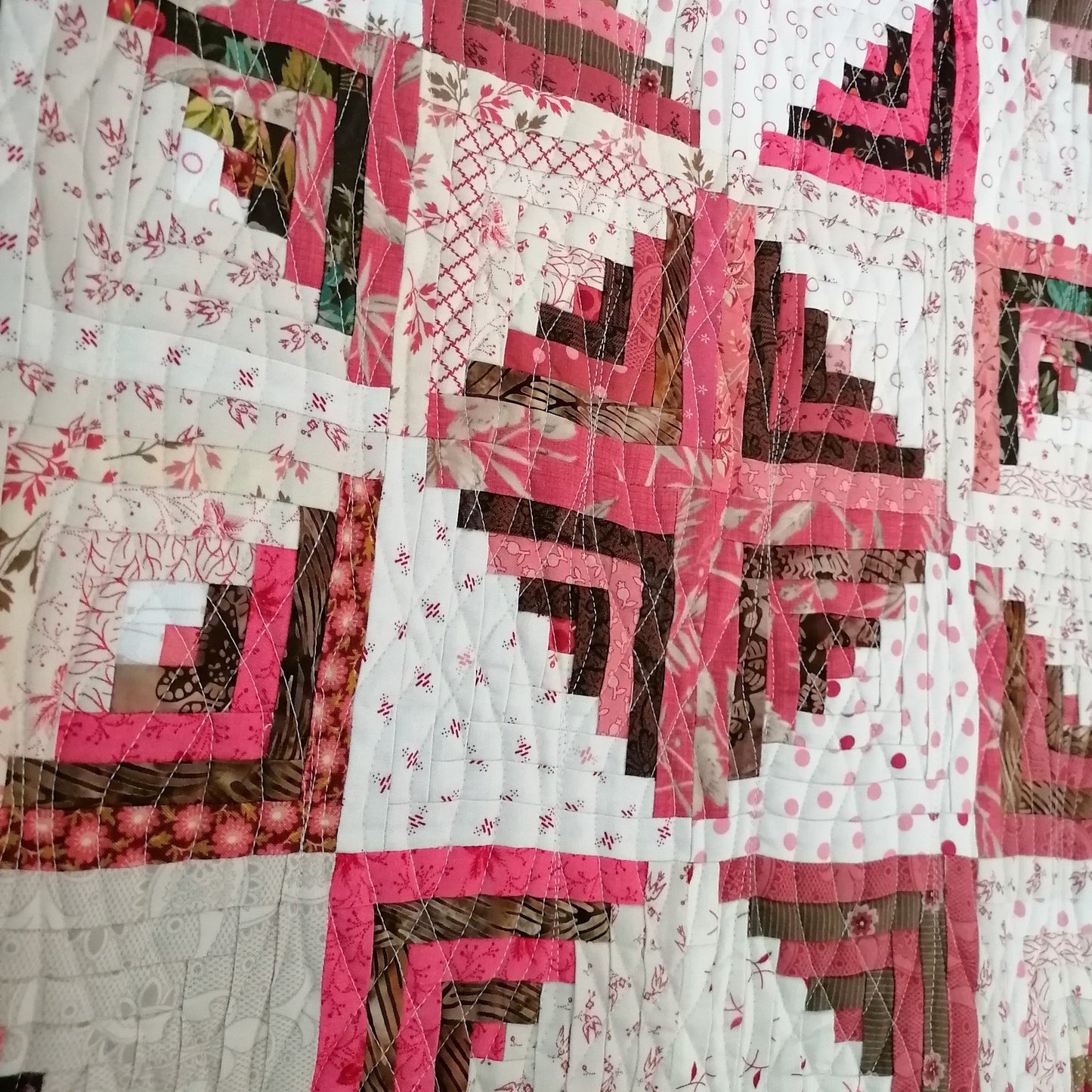 Patchwork quilt with pink, brown, and white patterns hanging on a rack.