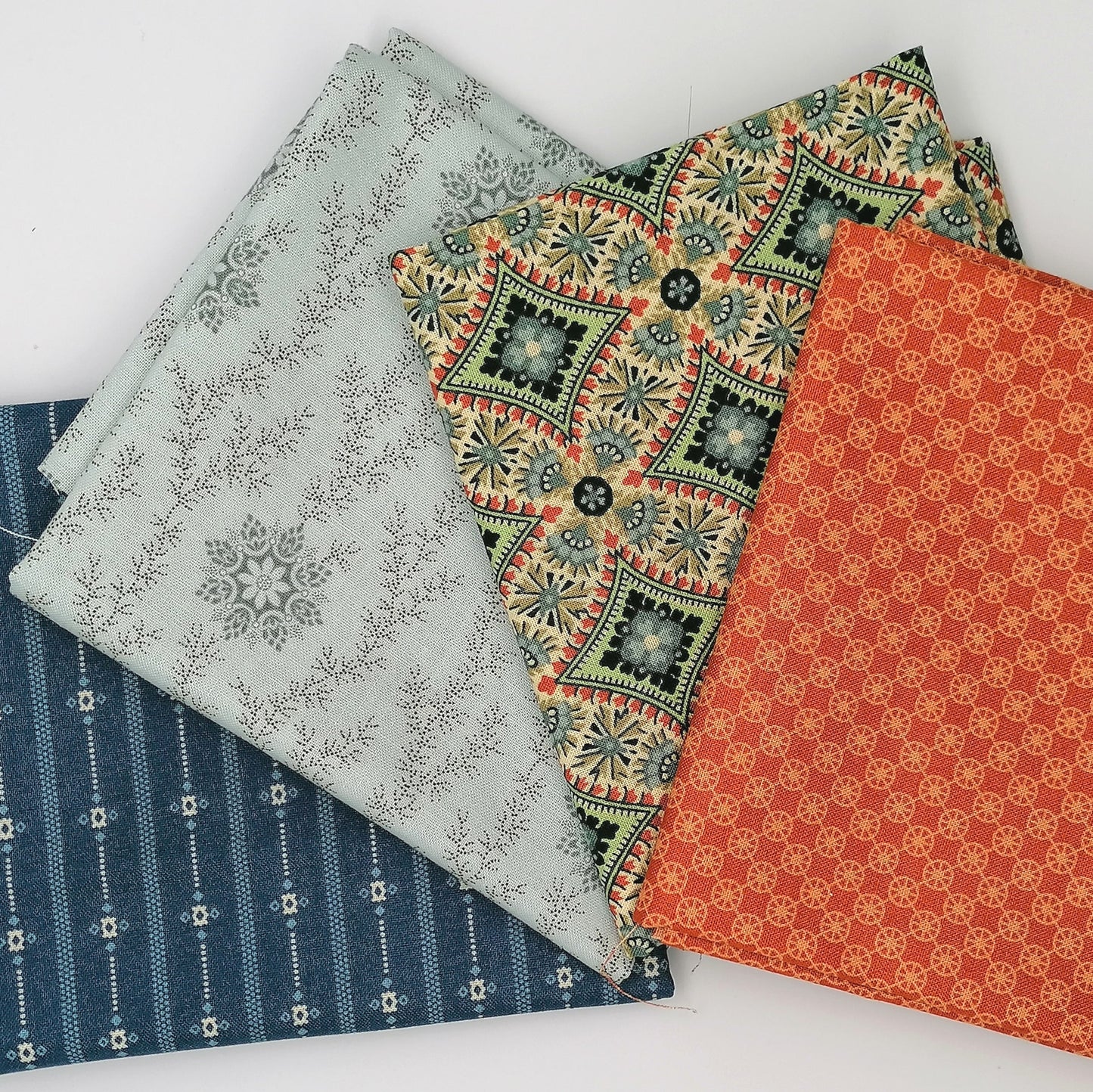 Fat Quarter Bundle LBQ25 - stacked flat lay showing orange circle print, cream tan medallion, pale grey ditsy vine, and navy stripe fat quarters from Laundry Basket Quilts for Andover Fabrics