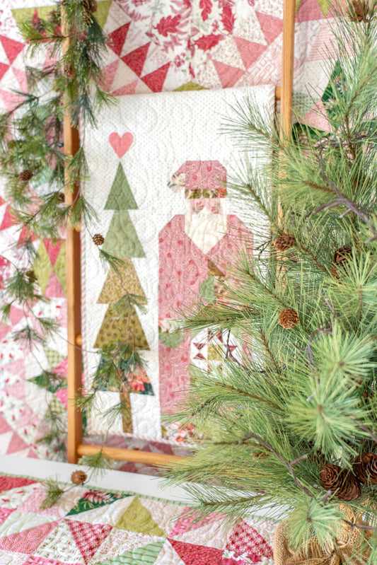Quilt with Christmas design featuring trees and Santa Claus, surrounded by greenery.