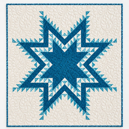 A blue and cream quilted wall hanging with a large geometric star motif is displayed on a white wall above a wire basket holding matching folded quilts in blue and cream tones.