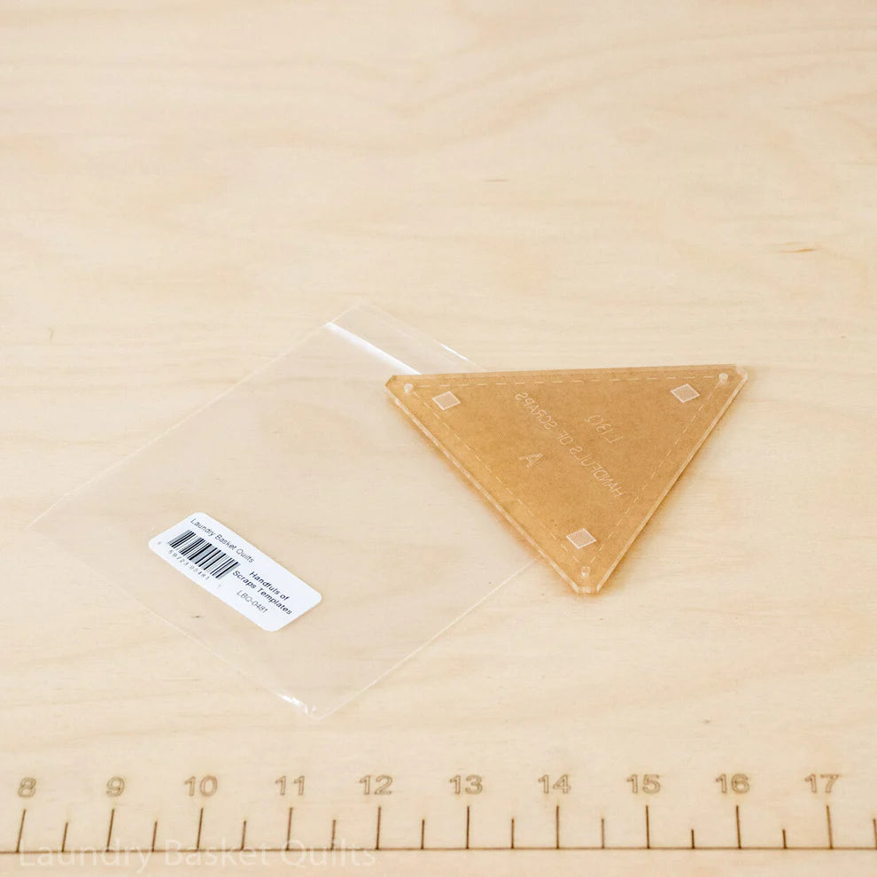 A triangular acrylic block with a clear plastic sleeve and a white barcode label, placed on a light wood surface with a ruler visible at the bottom.
