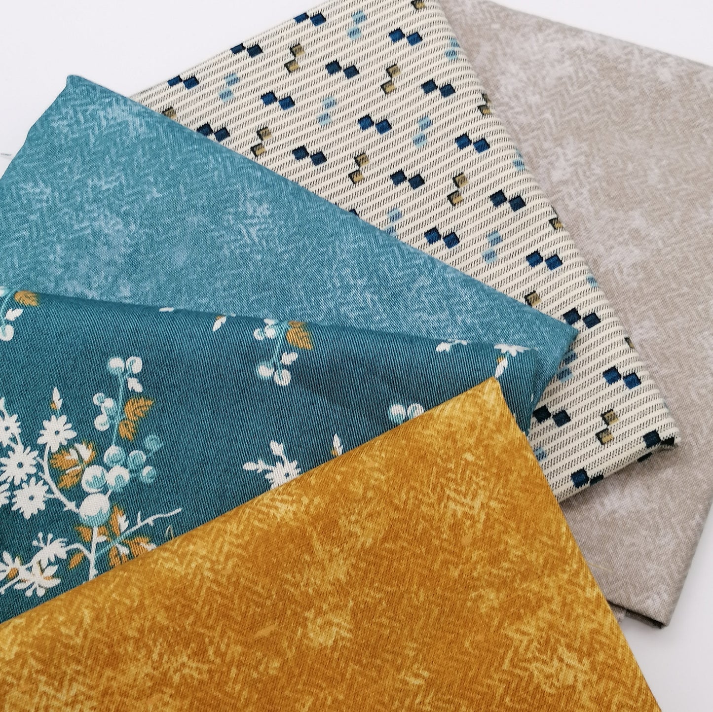 Fat Quarter Bundle LBQ17 - 5 fat quarters stacked showing warm grey, cream stripe with navy squares, teal solid, teal floral, and mustard gold from Laundry Basket Quilts