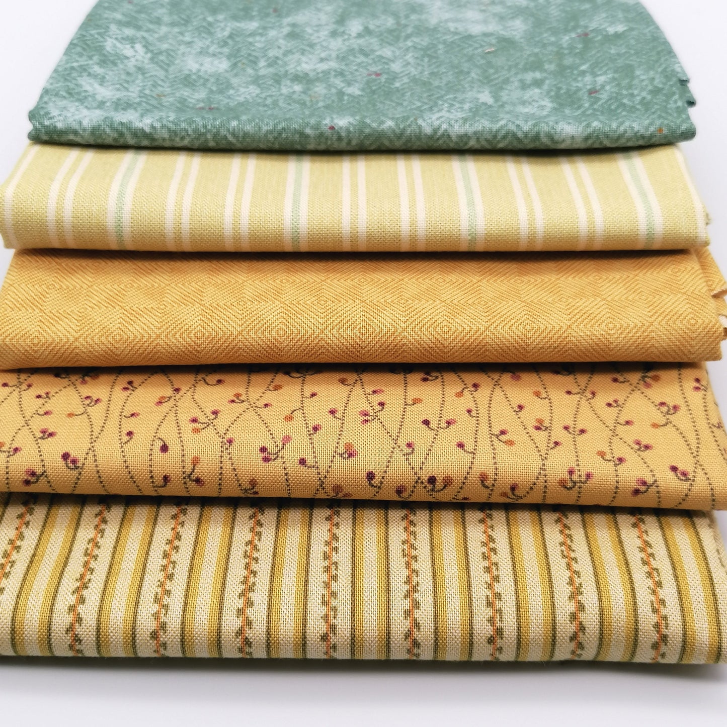 Fat Quarter Bundle LBQ20 - 5 fat quarters stacked showing sage mottled tonal, soft yellow cream stripe, mustard gold diamond geometric, golden sand burgundy floral vine, and cream gold multi-stripe from Laundry Basket Quilts