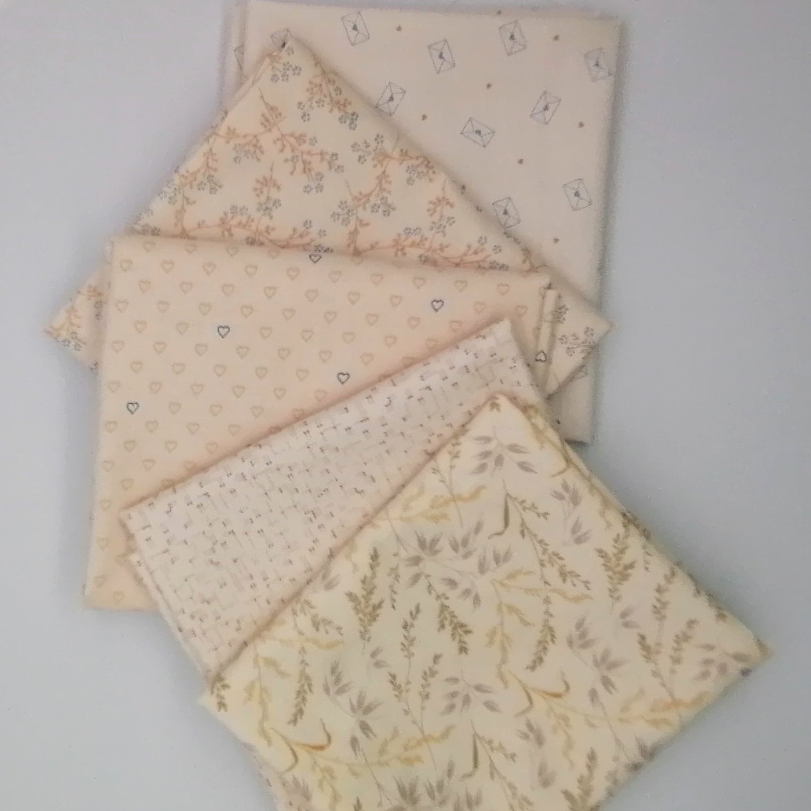 Fat Quarter Bundle LBQ21 - 5 fat quarters fanned showing cream botanical grasses, blush grid texture, blush hearts, blush ditsy floral branch, and cream letter envelope prints from Laundry Basket Quilts