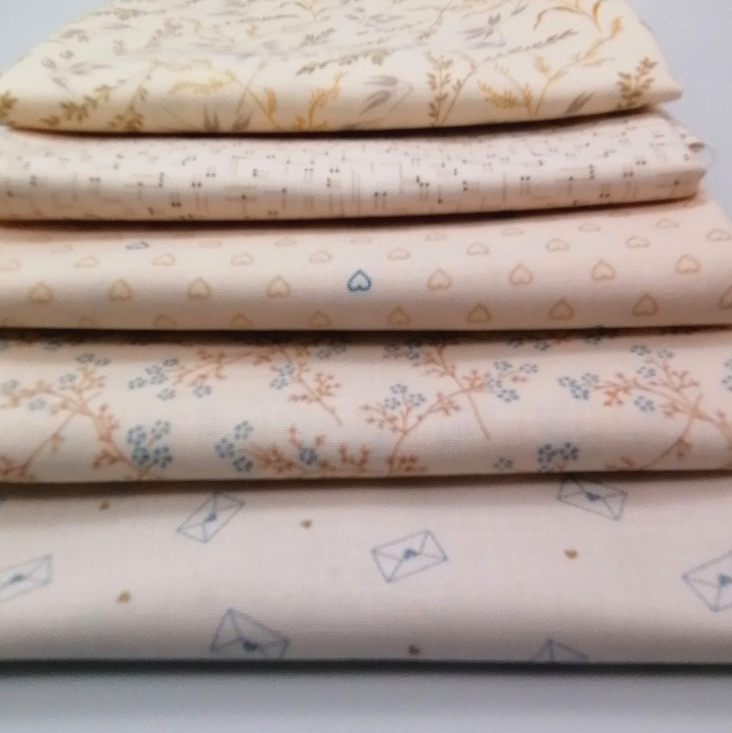 Fat Quarter Bundle LBQ21 - stacked fat quarters showing cream botanical, blush grid, blush hearts, orange branch floral and cream envelope prints from Laundry Basket Quilts for Andover Fabrics