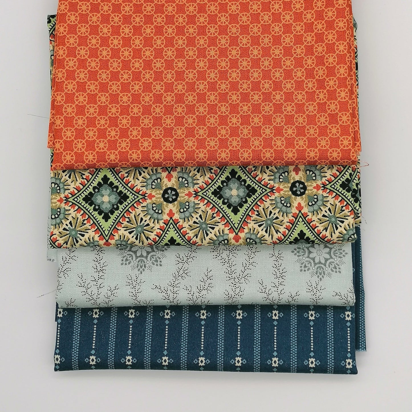 Fat Quarter Bundle LBQ25 - 4 fat quarters fanned showing orange geometric, cream medallion with green and red accents, pale grey floral vine, and navy stripe from Laundry Basket Quilts