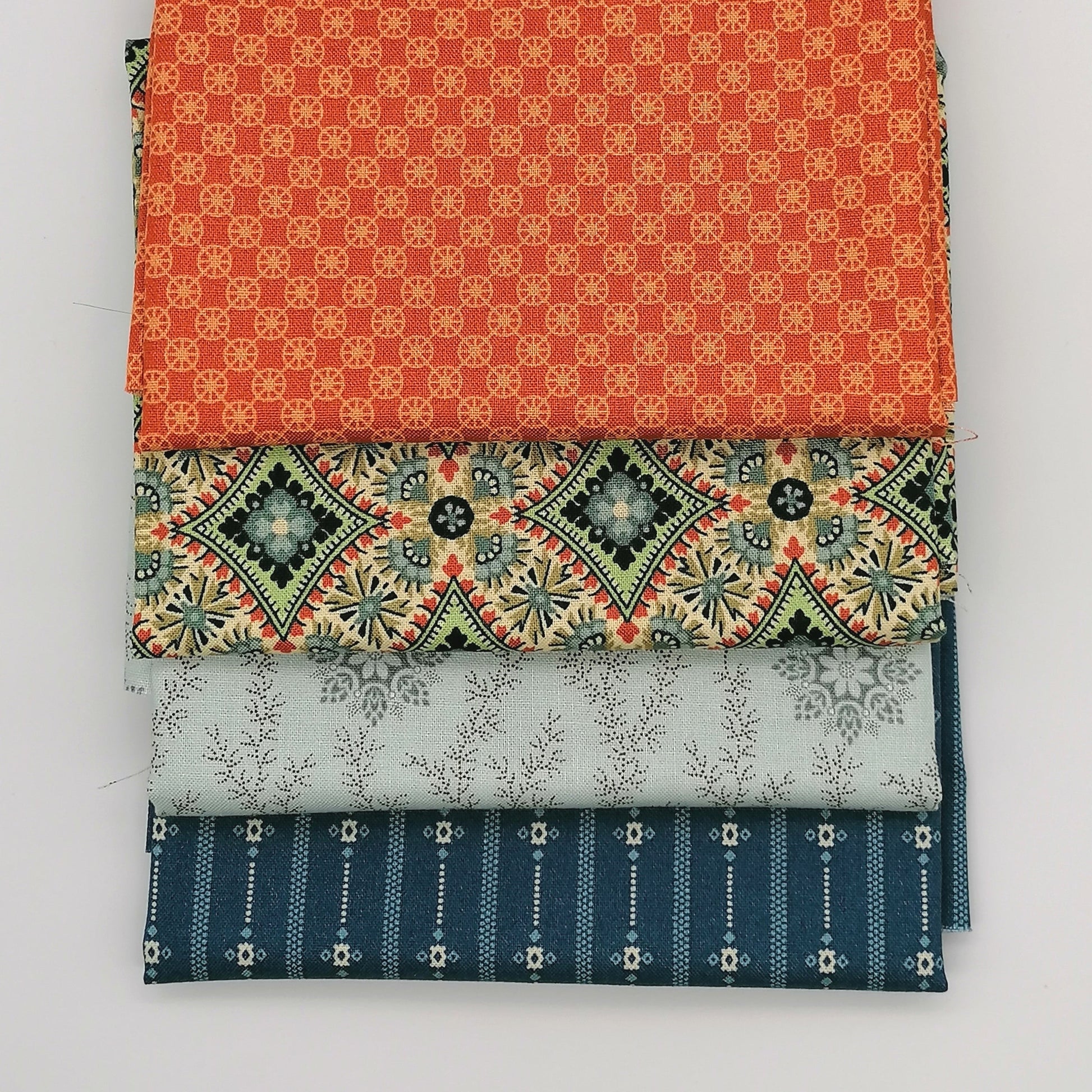 Fat Quarter Bundle LBQ25 - 4 fat quarters fanned showing orange geometric, cream medallion with green and red accents, pale grey floral vine, and navy stripe from Laundry Basket Quilts