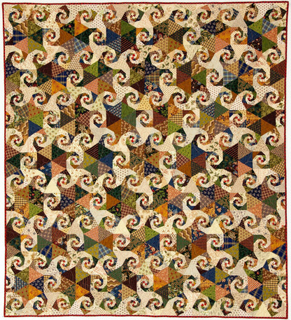 A vintage-style patchwork quilt featuring a repeating swirl pattern made from many small fabric triangles in earthy tones of brown, beige, blue, green, orange, and cream, finished with a red border.