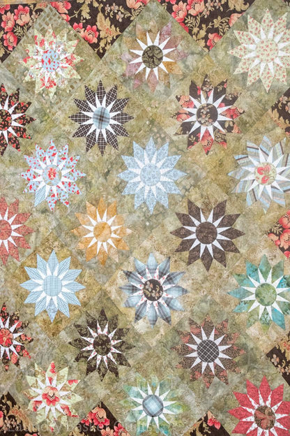 A close-up of a quilted fabric featuring a repeating pattern of multi-colored starburst and floral quilt blocks on a textured beige background.
