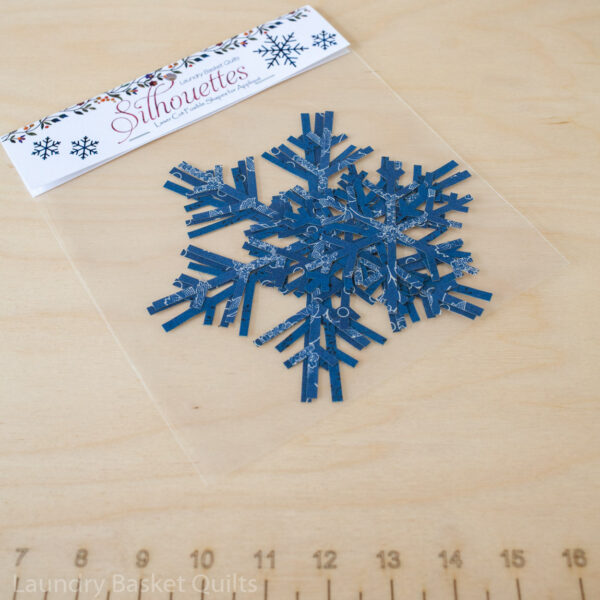 A package of 6 laser-cut snowflake fabric silhouettes in blue, featuring 3 large and 3 small snowflakes, pre-fused and ready for quilting. Perfect for winter-themed projects like the Sleigh Trio Pattern and Winter Village quilt.